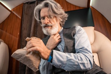 Yetişkin bir adam özel uçakta kusmuk torbası taşıyor.