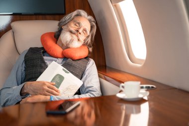 Uçakta kahve ve akıllı telefonun yanında uyurken boyun yastığı tutan bir iş adamı. 
