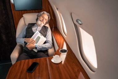 Özel uçakta akıllı telefon ve kahvenin yanında uyuyan işadamı dergisi tutuyor. 