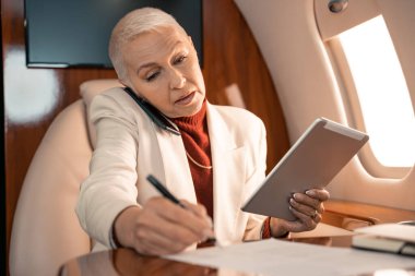 Kağıda dijital tablet yazan ve özel uçakta akıllı telefondan konuşan bir iş kadını. 