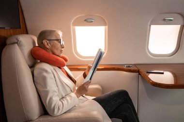 Uçakta akıllı telefonun yanında boyun yastığı okuyan iş kadınının yan görüntüsü. 