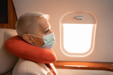 Sağlık maskeli ve boyun yastıklı bir iş kadını jet 'te oturuyor. 
