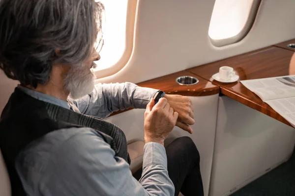 飛行機の中でスマートウォッチを見て成熟したビジネスマン — ストック写真