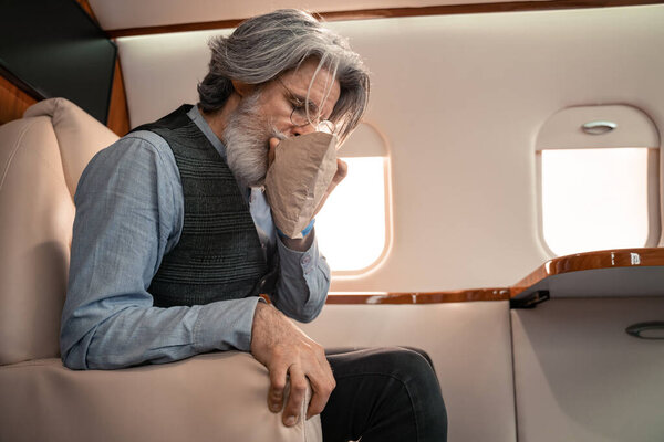 Mature man breathing in air sickness bag in private jet 