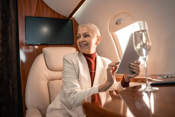 飛行機の中でぼやけたシャンパンの近くでデジタルタブレットを使用して笑顔ビジネス女性 — ストック写真