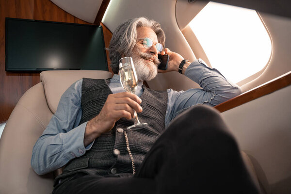 Low angle view of smiling businessman talking on smartphone and holding champagne in plane 