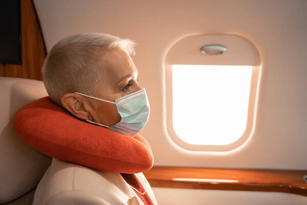 Businesswoman in medical mask and neck pillow sitting in jet 