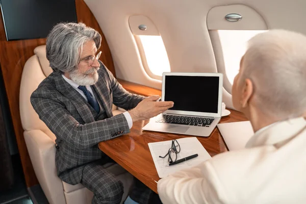 商人指着靠近纸张的笔记本电脑 在私人飞机上模糊的女商人 — 图库照片