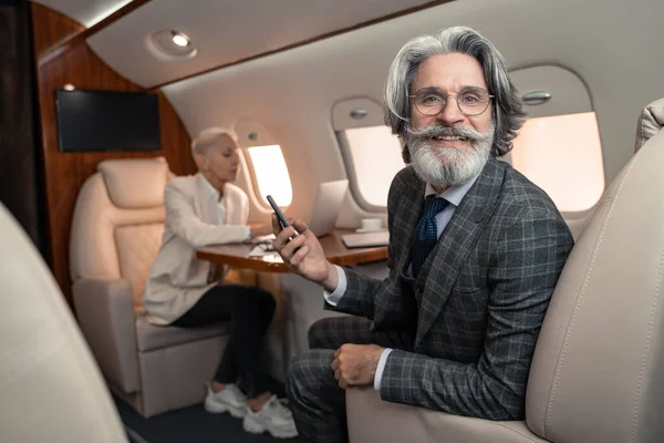Empresário Sorridente Segurando Smartphone Perto Parceiro Negócios Desfocado Avião Privado — Fotografia de Stock