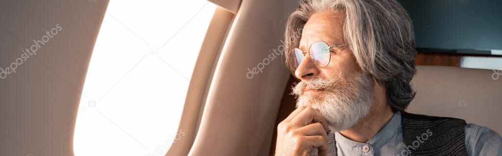 Mature man in eyeglasses looking at airplane window, banner 