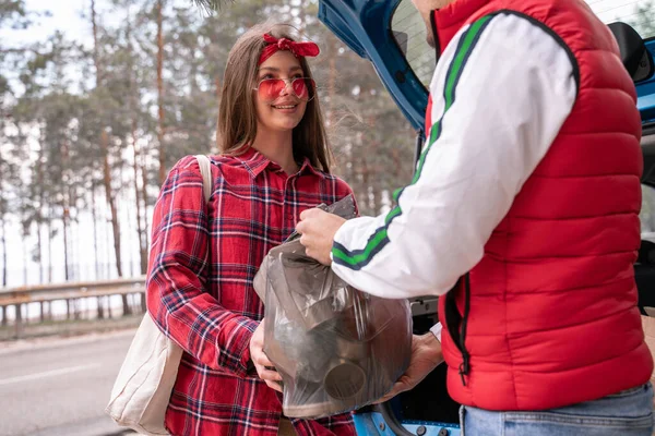 サングラスの幸せな若い女性と森の中で車の近くにゴミ袋を持っている男 — ストック写真