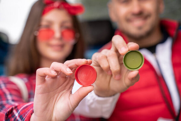 blurred man and woman holding plastic bottle caps 