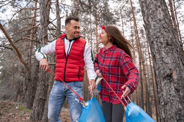 ゴミ袋を持った幸せなカップルが森の中で道具を持ってゴミを拾い — ストック写真