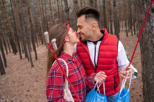 happy couple with trash bags holding pick up tools and kissing in forest
