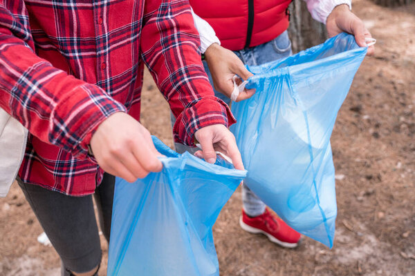partial view of man and woman holding blue trash bags 
