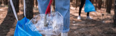 cropped view of volunteer picking up rubbish in forest, banner clipart