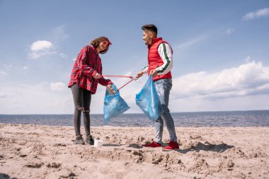Çöp torbaları ve kapkaççıları olan mutlu çift kumda çöp topluyor. 