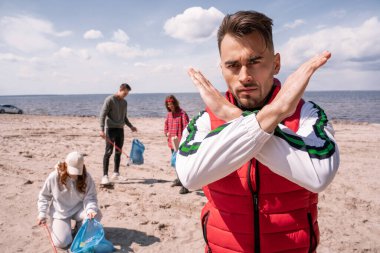 man showing stop gesture near group of volunteers picking up trash, ecology concept  clipart