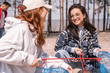 happy young women with grabbers picking up garbage outside  clipart