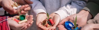 Elinde pil, plastik şişe kapağı ve yeşil bitkiler tutan gönüllülerin kırpılmış görüntüsü.
