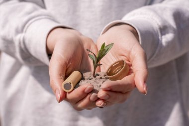 Elinde pil, plastik başlık ve yeşil bitki tutan bir kadın.