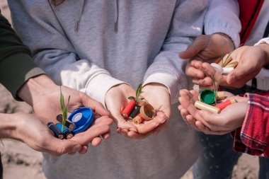 cropped view of volunteers holding batteries, plastic bottle caps and green plants in hands  clipart