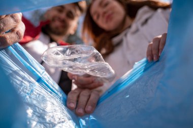 Bulanık gönüllülerin yanındaki çöp torbasına düşen plastik bardak.