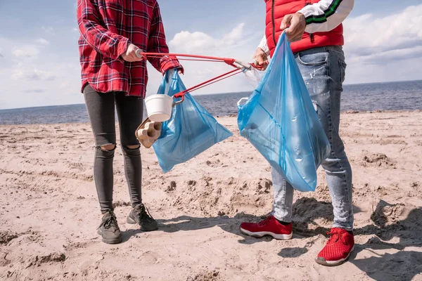 Vista Recortada Pareja Con Bolsas Basura Agarradores Recogiendo Basura Arena — Foto de Stock