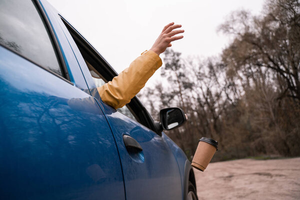 cropped view of man throwing away empty paper cup from blue car