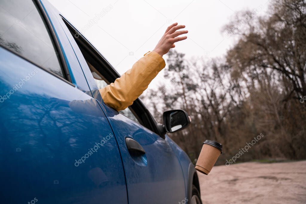 cropped view of man throwing away empty paper cup from blue car