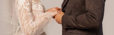 partial view of bride and groom holding hands isolated on grey, banner