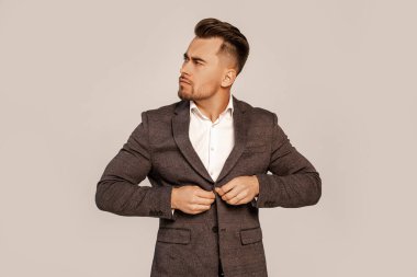confident man looking away while buttoning blazer isolated on grey with lilac shade