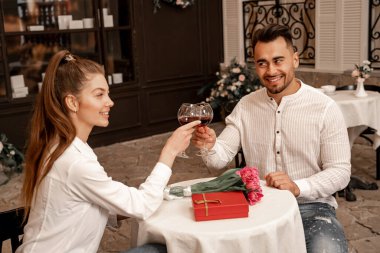 happy couple clinking wine glasses near gift box and tulips in cafe