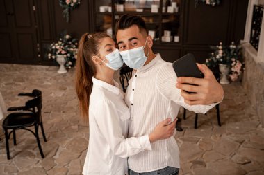 woman in medical mask embracing man taking selfie in restaurant