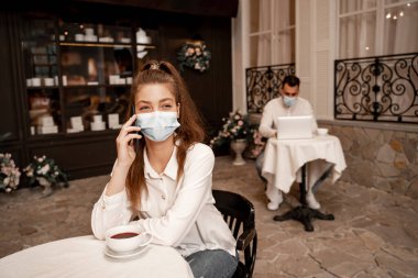 young woman talking on smartphone near man working on laptop on blurred background