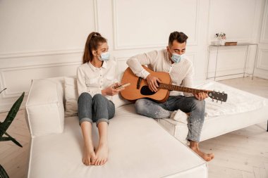 couple in medical masks and casual clothes playing mbira and acoustic guitar at home