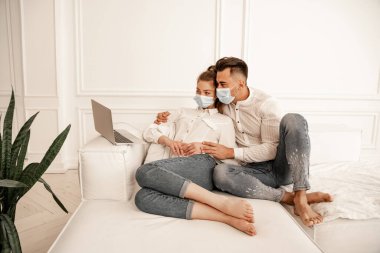 man in medical mask hugging girlfriend while watching movie on laptop