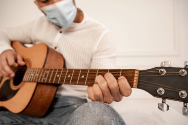 cropped view of blurred man in medical mask playing guitar at home