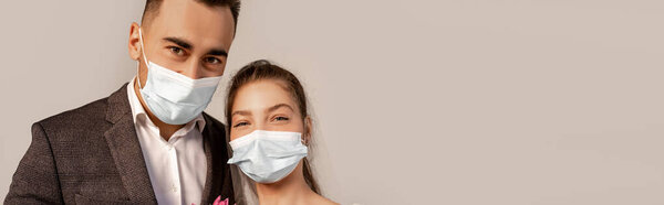 young bride and groom in medical masks looking at camera isolated on grey with lilac shade, banner