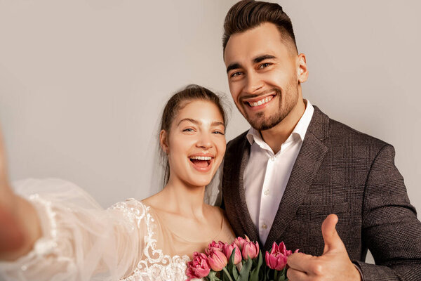 happy man showing thumb up near excited bride isolated on grey