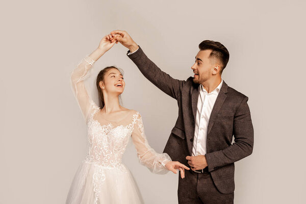 happy young newlyweds dancing isolated on grey with lilac shade