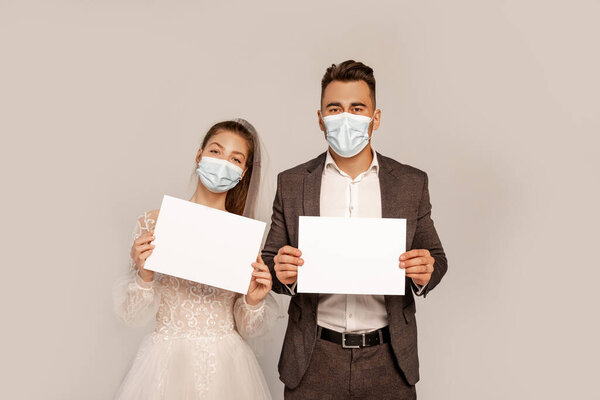 young couple in medical masks holding blank placards isolated on grey