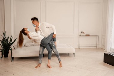 young couple in safety masks and jeans dancing in living room