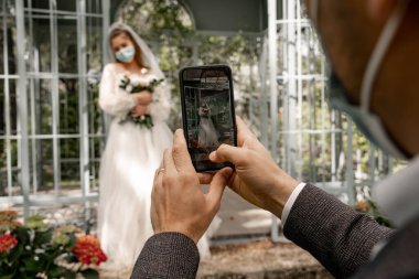 selective focus of smartphone in hands of groom taking photo of bride