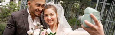 happy bride taking photo with groom on digital camera outdoors, banner