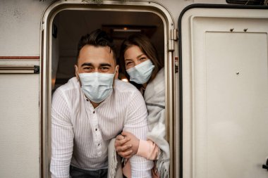 positive young couple in medical masks looking out camper