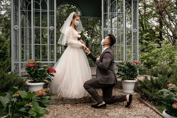 Mann Mit Medizinischer Maske Steht Kniend Neben Eleganter Braut Park — Stockfoto