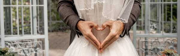 cropped view of man showing heart sign with hands while hugging bride, banner