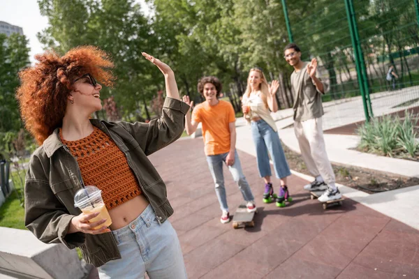 Young Excited Woman Refreshing Drink Waving Hand Blurred Multiethnic Skaters — Stock Photo, Image