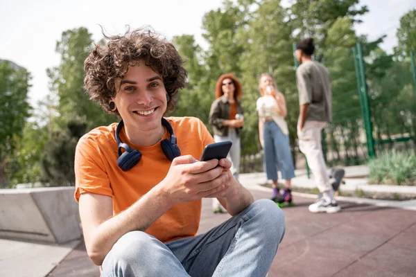 Curly Man Mobile Phone Smiling Camera Blurred Multiethnic Skaters — Stock Photo, Image